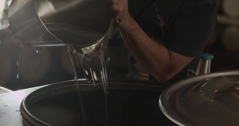 A man pours a bucket of water into distillery equipment