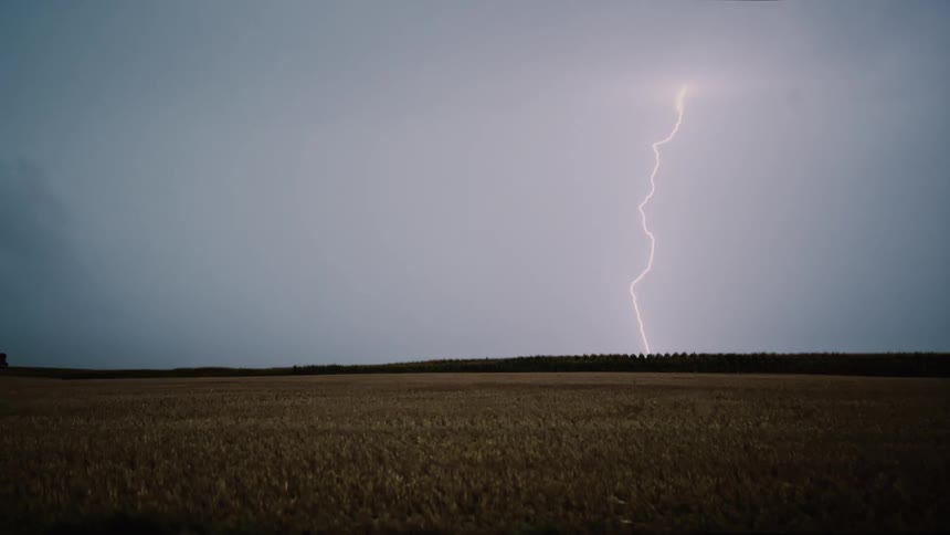The long green field has a heavy storm moving ahead