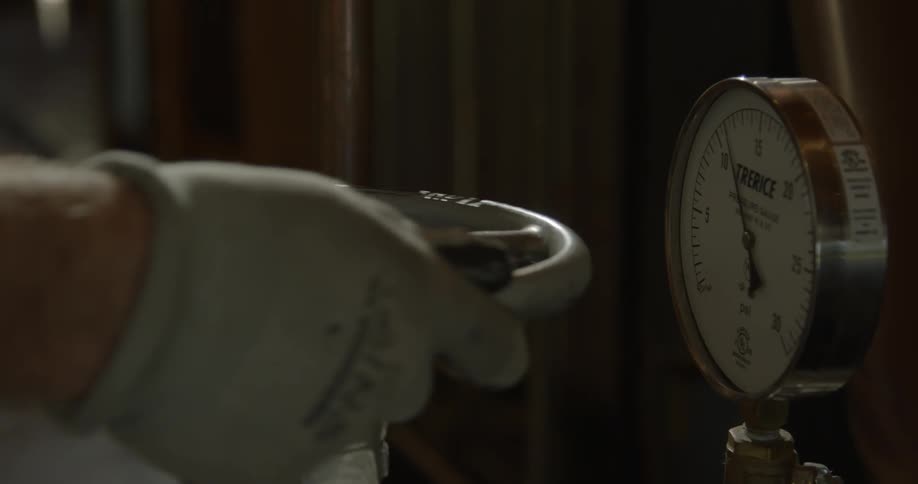A man wearing work gloves turns a gear and checks a gauge