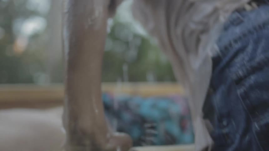 A man wearing denim shorts and a t shirt struggles to climb out of a lake