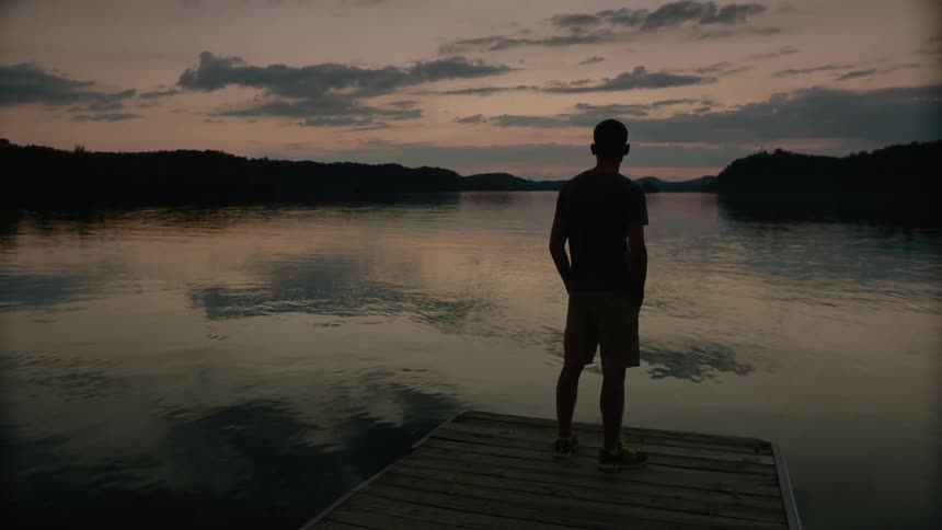 Man standing on a pier by the water at sunset