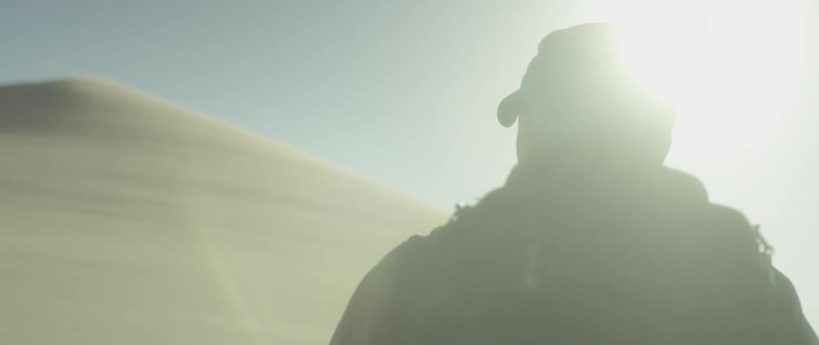 Man walking on a windy desert with the sun up high