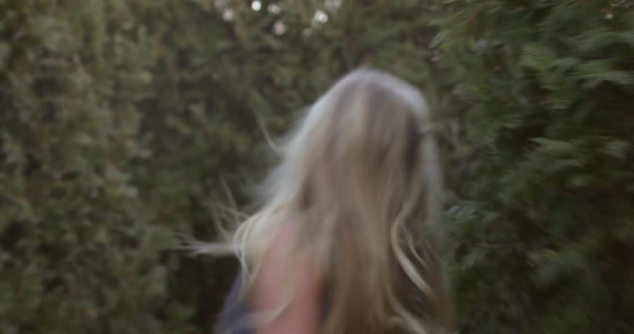 Blonde woman running through a maze made up of tall bushes