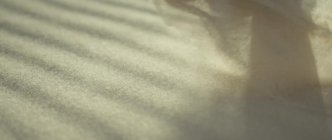 A white man walks barefoot on a sand dune