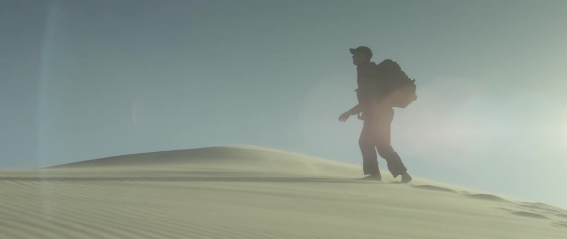 Man with backpack trudges through desert sand