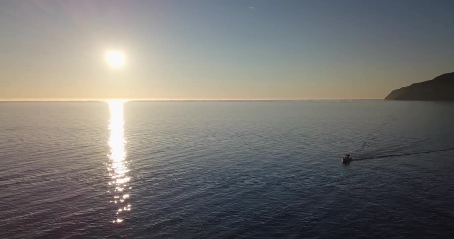 A boat floats on the rippling ocean at sunset