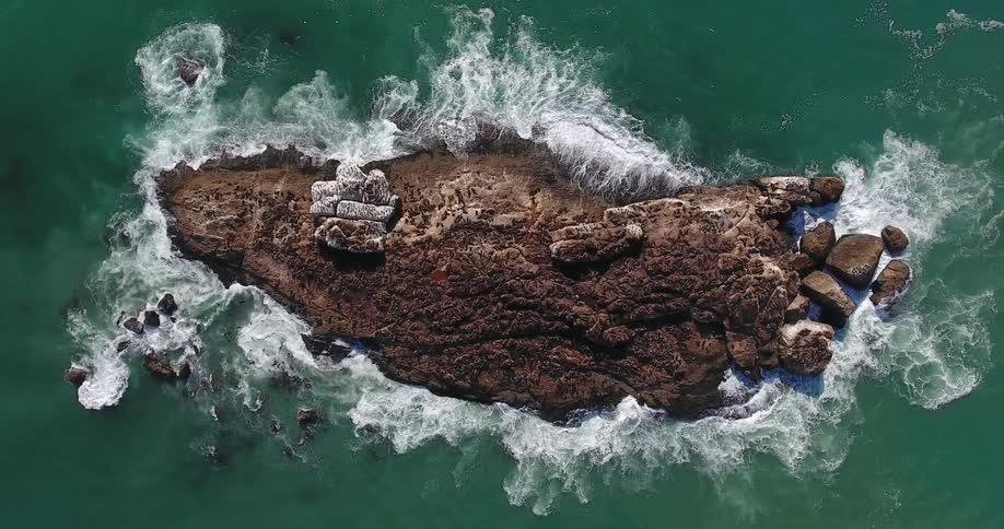 Waves crash around and lap a tiny rock island