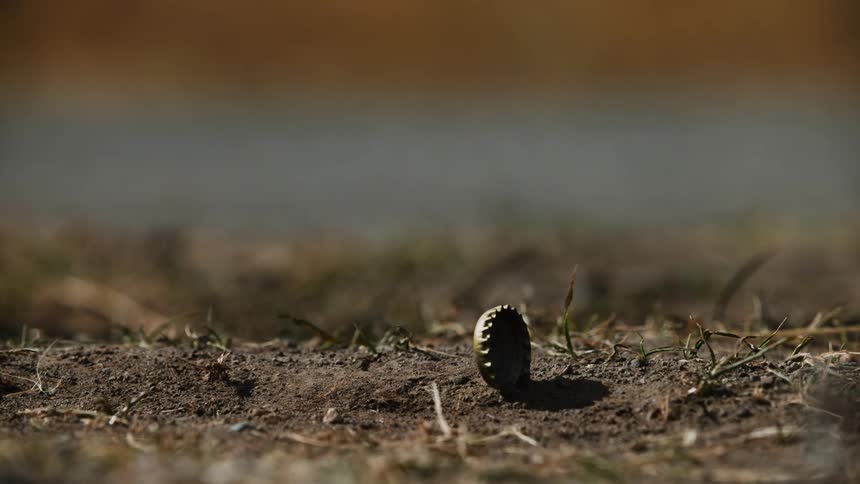 Bottle cap rolls on the dirt ground