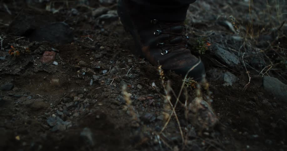 A person in boots walks across rocky ground