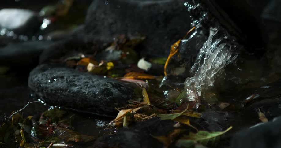 A man's booted foot lifts up out of the water in a rocky creek bed