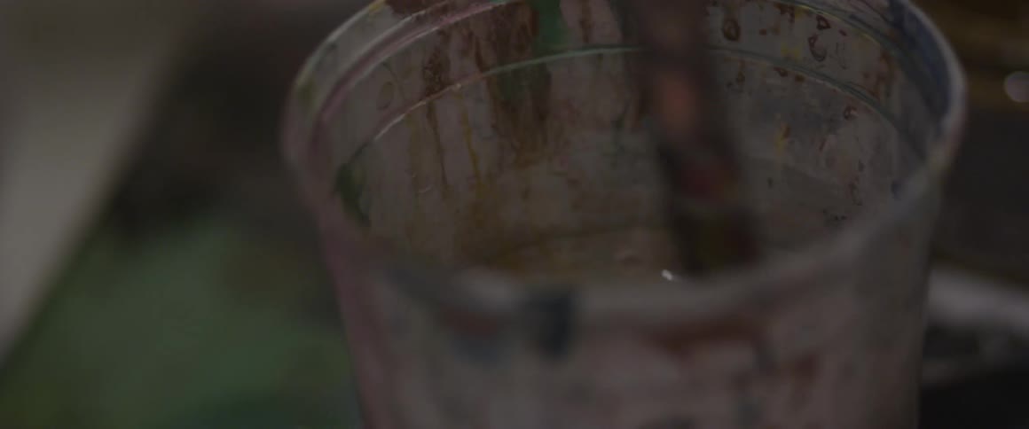 A man cleaning a paint brush in a cup of water