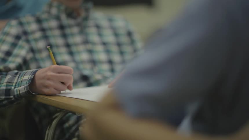 People sitting at desks one is writing with a pencil