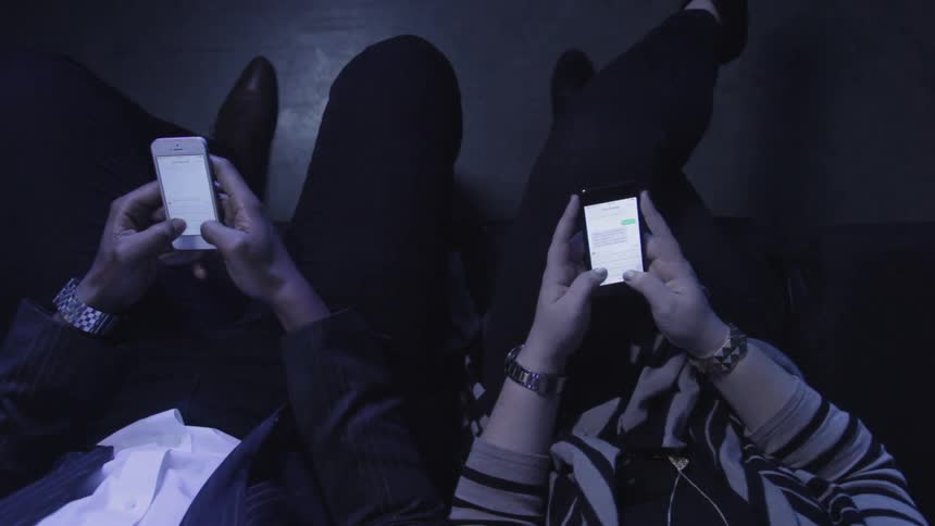 Two people are sitting next to each other using their cell phones