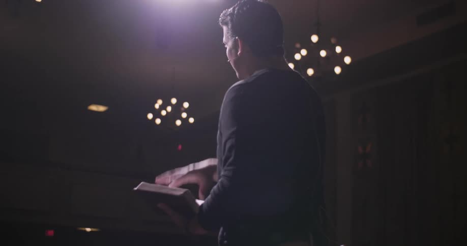 Man stands on a stage reading a book out loud