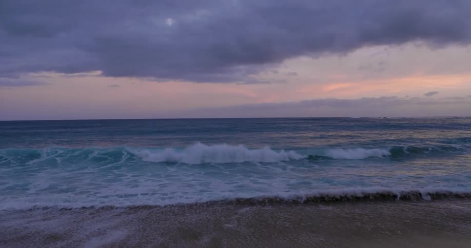 Ocean waves wash ashore a sandy beach at sunset