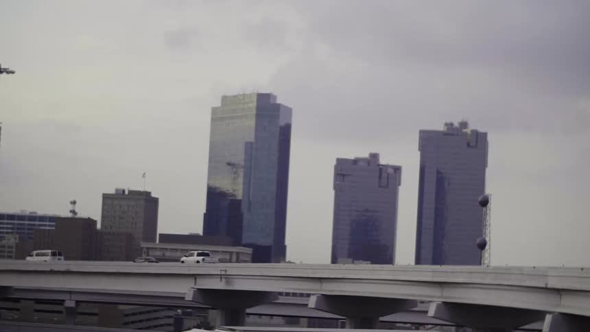 Cars driving on a highway in front of tall buildings on a cloudy day