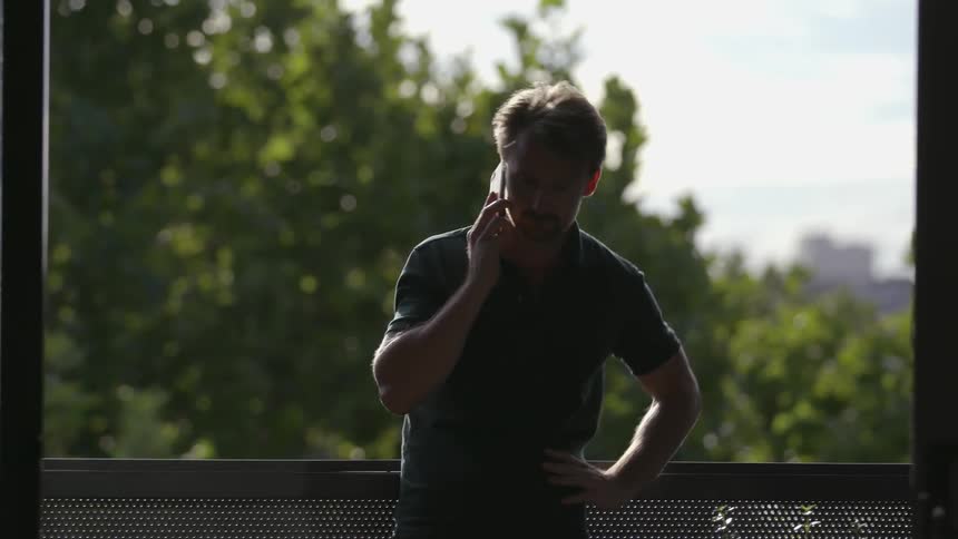 A man leans against the balcony railing while talking on the phone