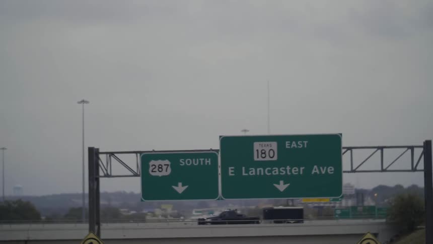 A truck towing a trailer travels on an overpass beyond freeway road signs