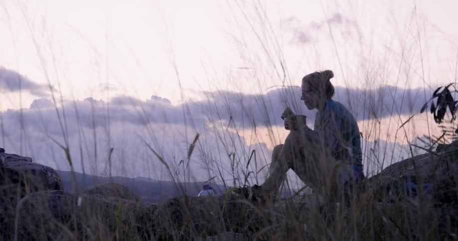 Woman eats out of a bowl sitting outside on a rock
