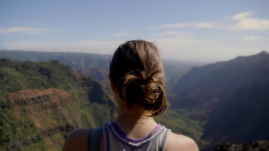 A woman stands viewing a canyon on a sunny day