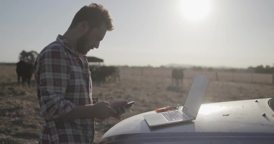 A man is using a laptop then picks up his phone outside