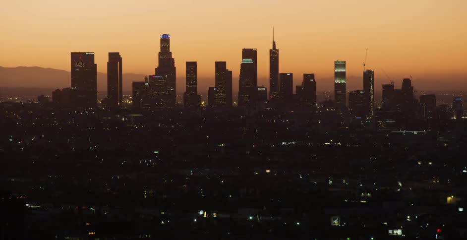 A cityscape with tall skyscrapers is shown at sunset
