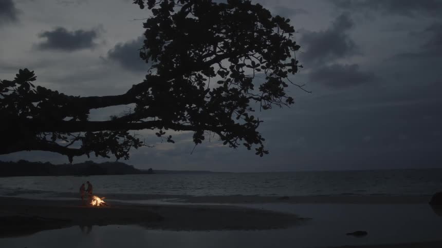 Man and woman kiss in front of a fire on the beach