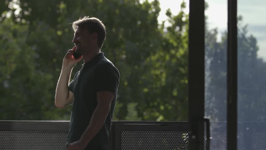 A man stands on a balcony and talks on the phone