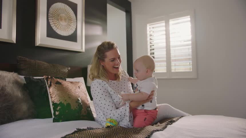 A mom laughing while holding her baby on the bed
