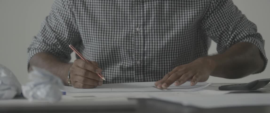 A man draws on a piece of paper at a desk