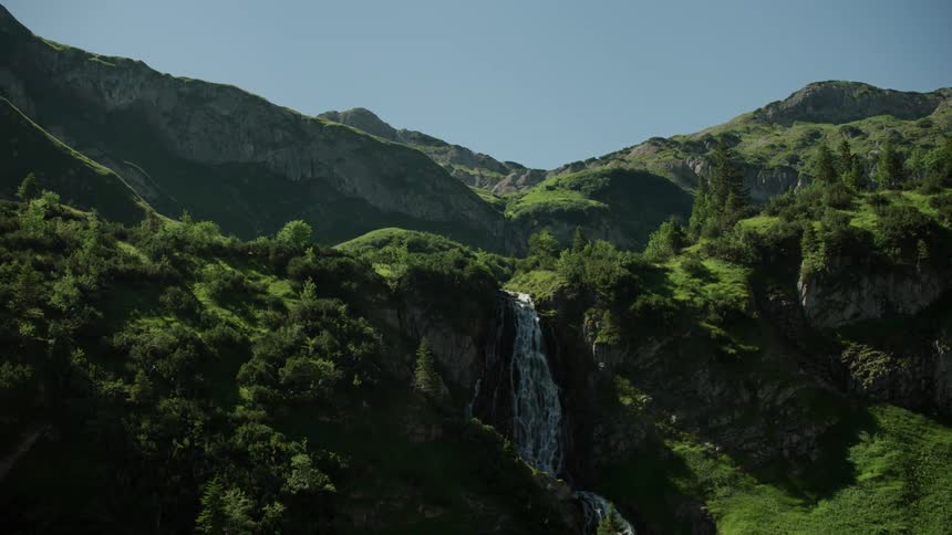 The sun shines on green mountain peaks and a waterfall