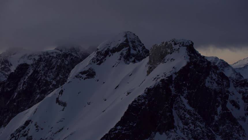Storm clouds are moving across a snow-covered mountain range