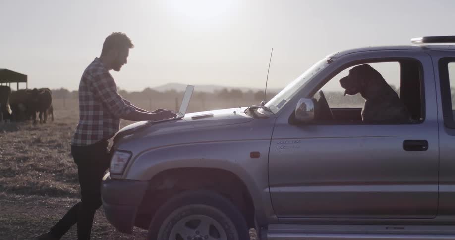 A man types on a laptop on the hood of his car