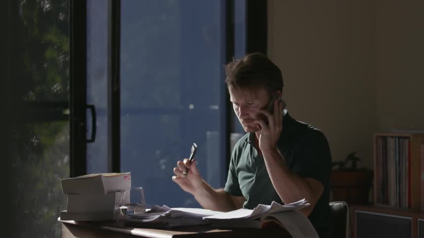A man flips through papers while talking on the phone