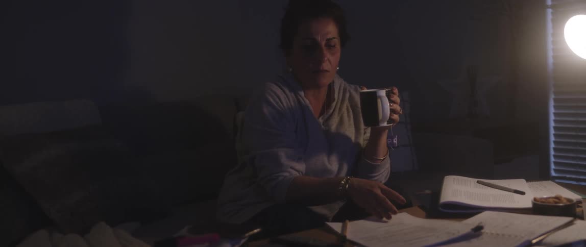 Woman sits on a couch with a mug of coffee and papers