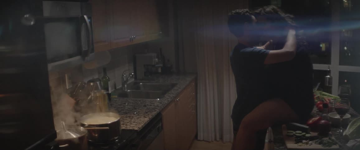 A woman sits on the kitchen counter as a man kisses her