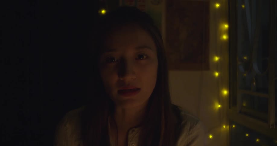 A woman in a dimly lit room talks and looks down