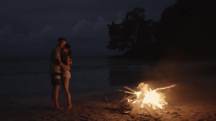 A couple embrace on a beach near a fire