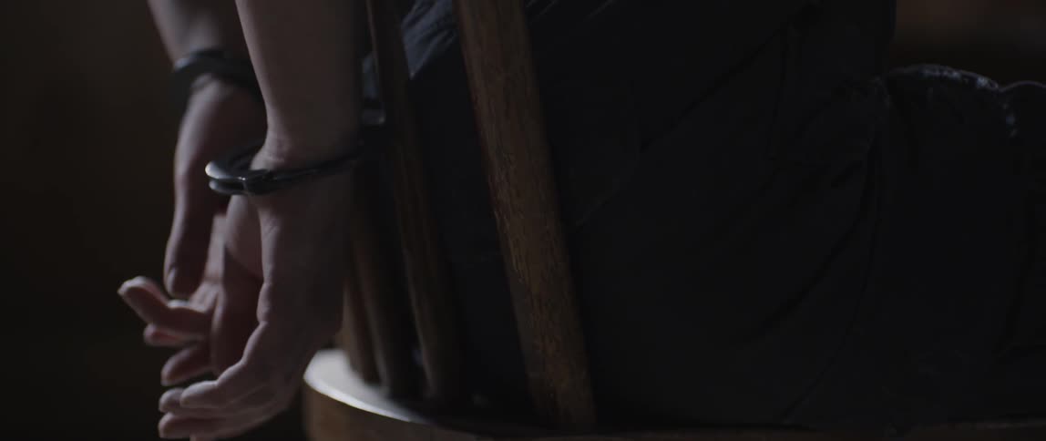 A person is sitting on a chair handcuffed from behind