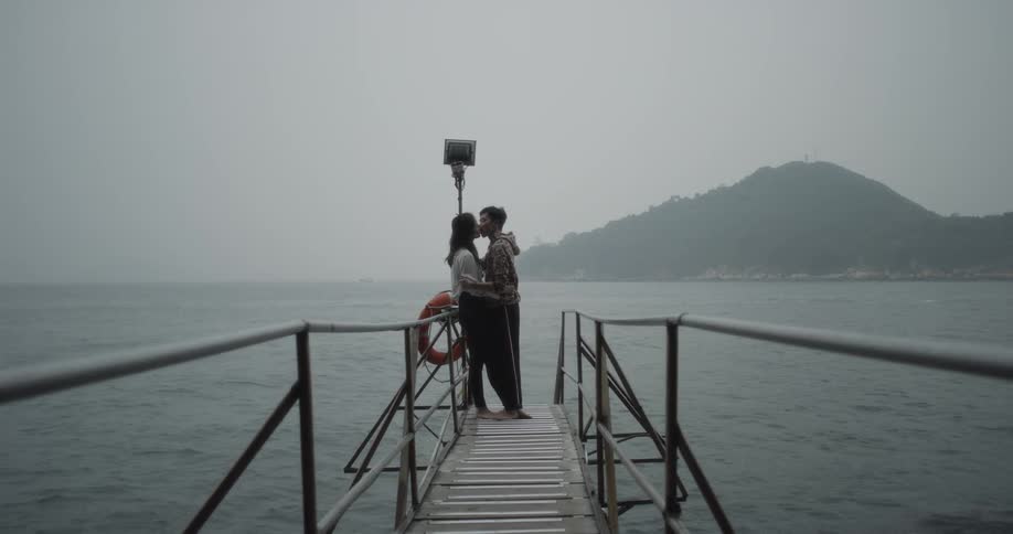 Man and woman kiss on dock on overcast evening