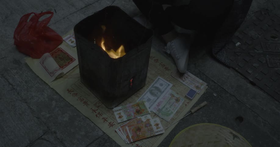 A person feeds money into a fire in a bin