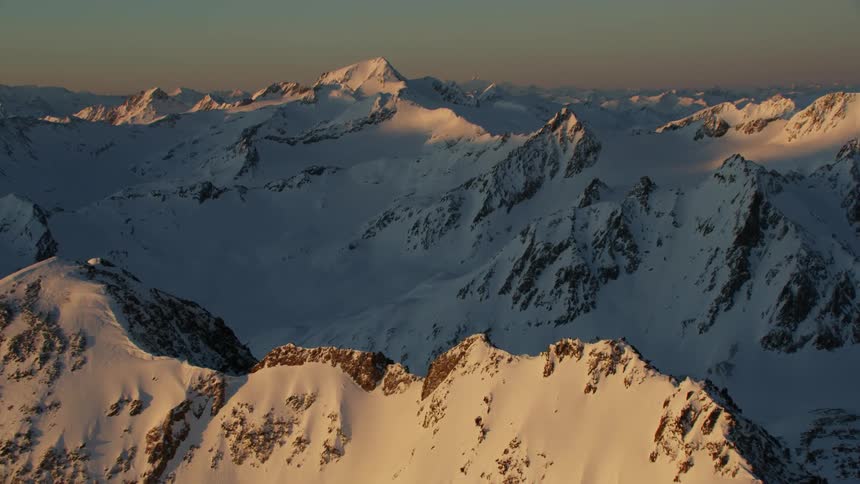 Snow covers rocky mountains at sunset