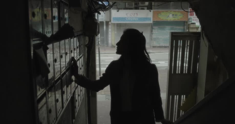 A woman walks into an apartment building and touches the mailboxes