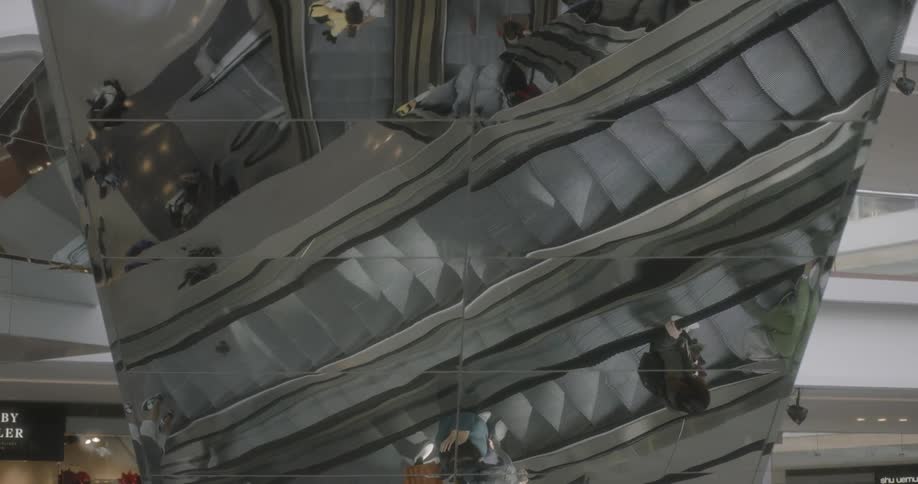 Reflection on a glass wall of people riding an escalator inside a building