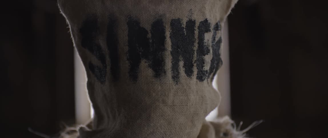 A person has a sack on their head that says sinner