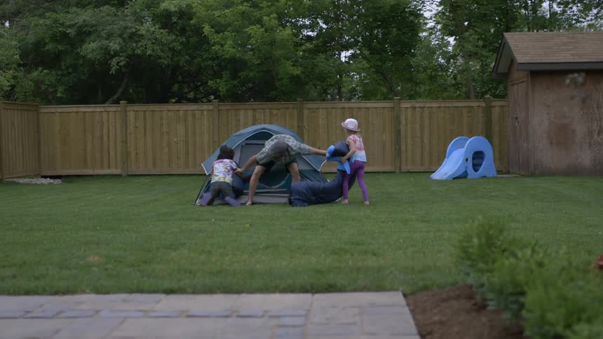 A man plays with children by a tent in the yard
