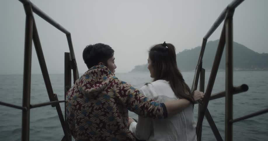 A man and woman sit on a pier by the water talking