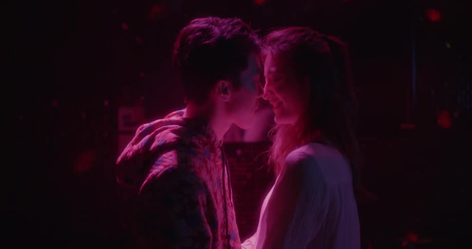 A man and woman kiss in a dark room with red lights