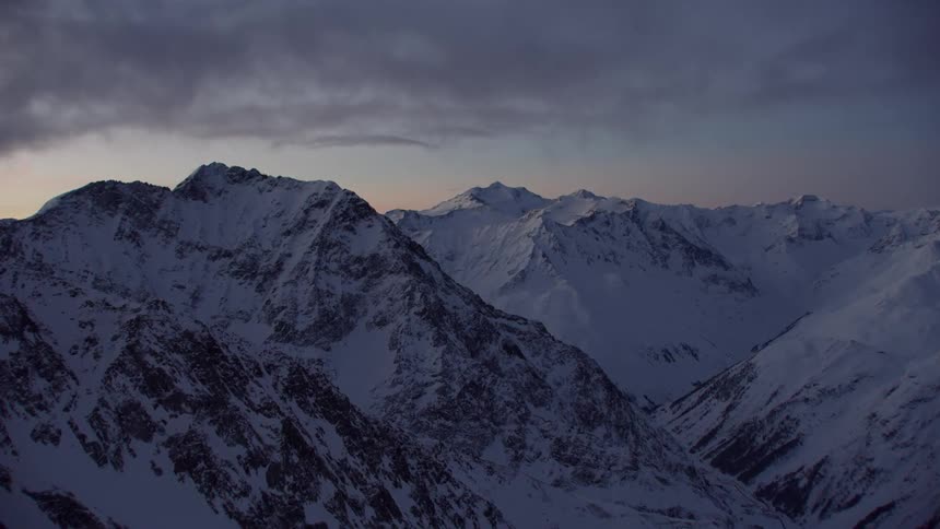 Clouds hang over snow covered peaks at sunset