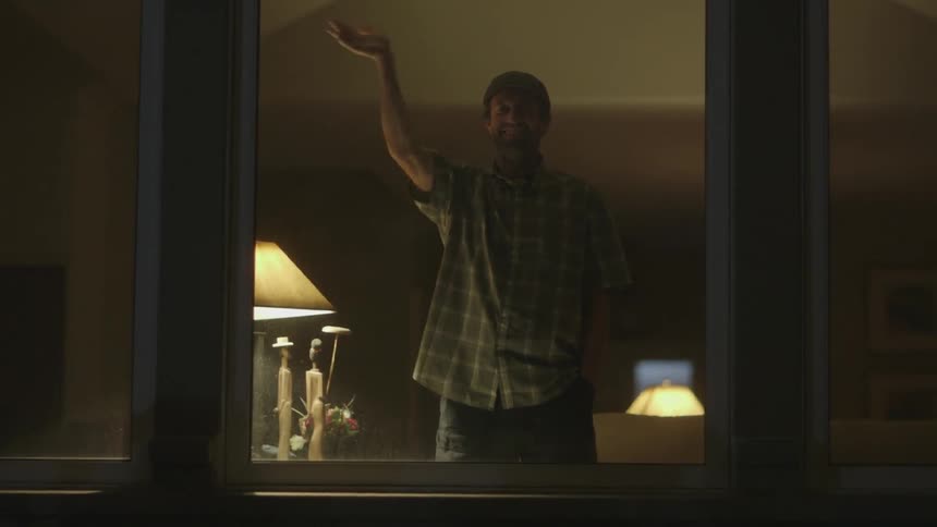 A man stands by the window waving